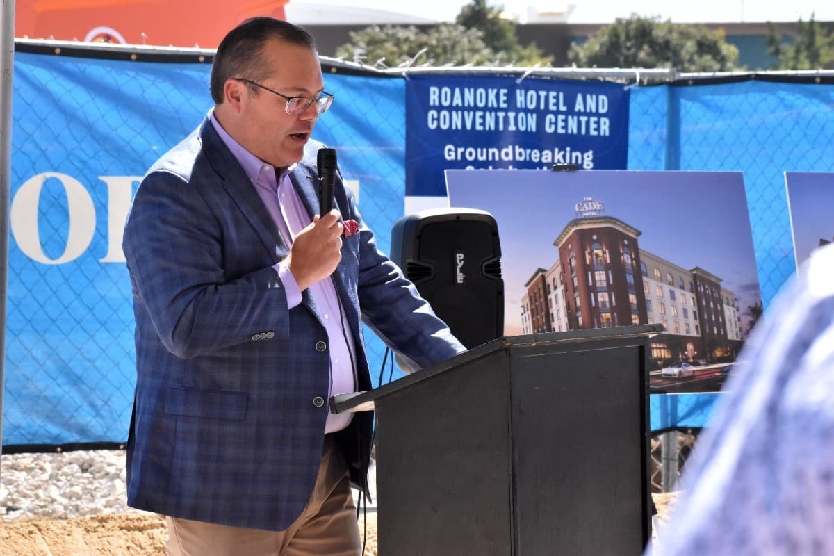 A speaker addresses attendees at the groundbreaking for The Cade Roanoke Hotel & Convention Center, with the hotel rendering displayed